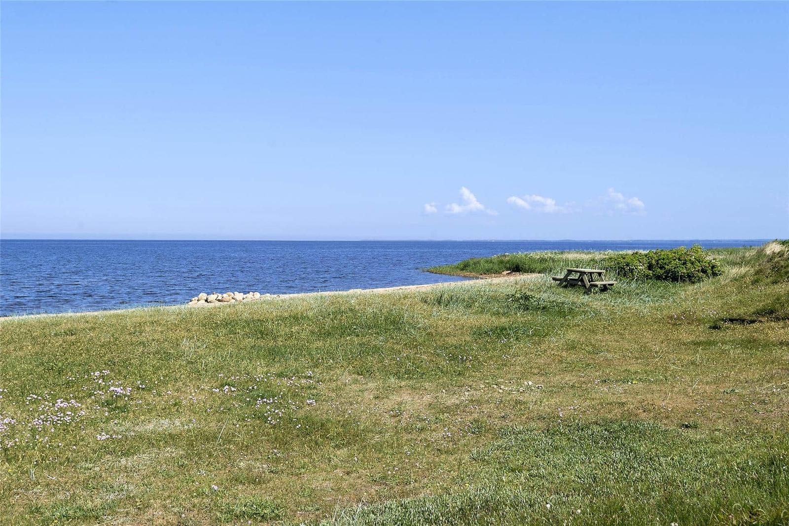Grünes Gras am Strand mit Picknicktisch und Blick auf das Meer unter blauem Himmel.