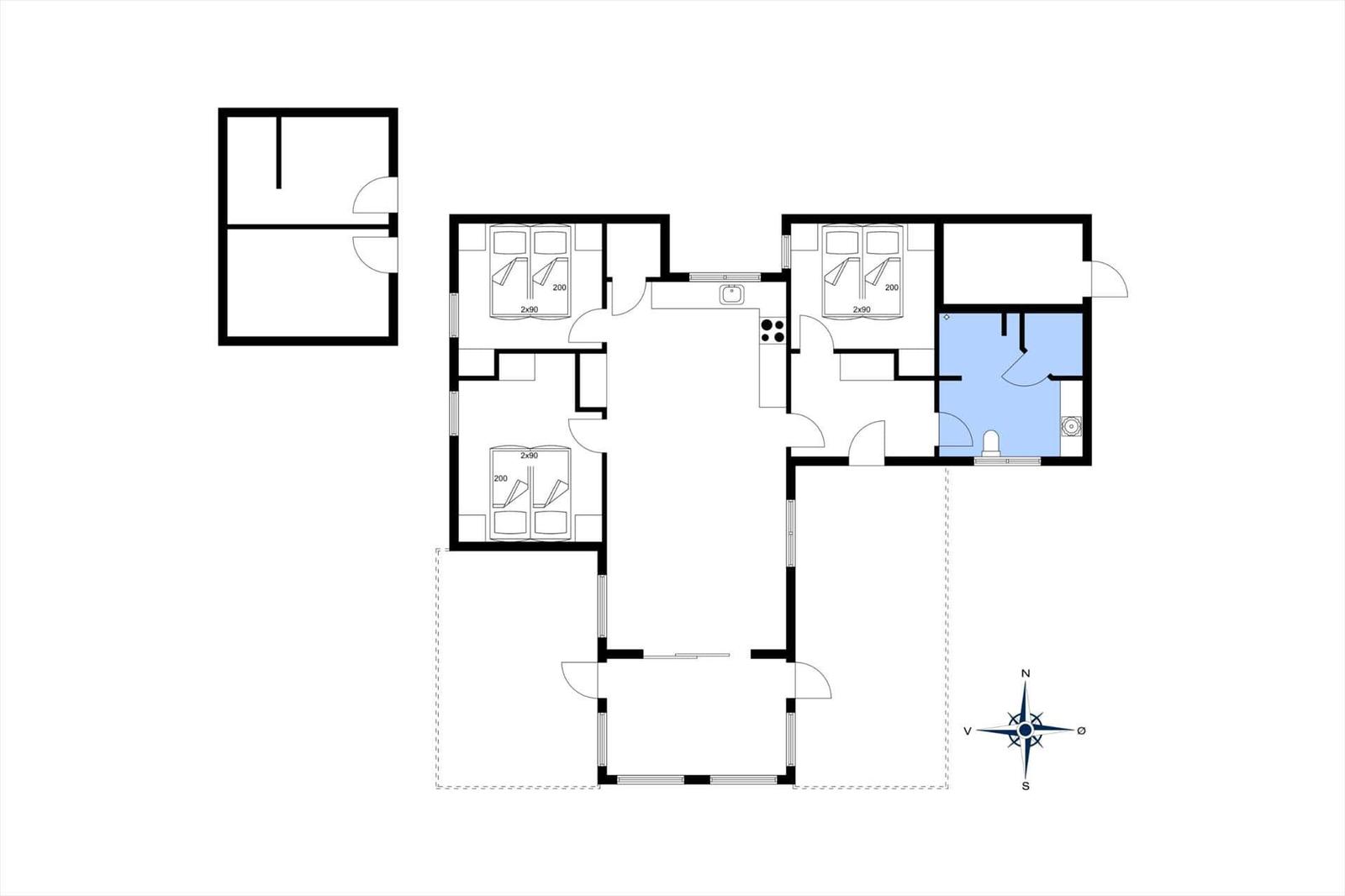 Strand mit Grasfläche und Holztischen. Im Hintergrund Wald und Wasser unter blauem Himmel.