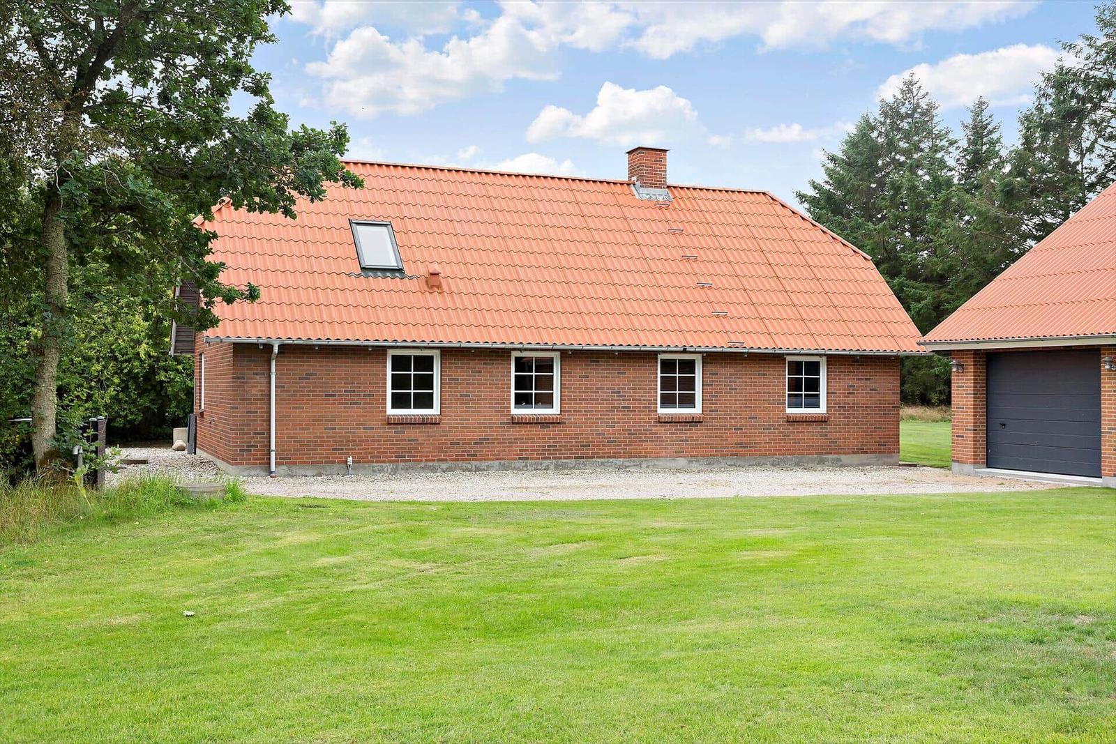 Rotes Dach, Backsteinhaus mit vier Fenstern und Garage. Grasfläche und Bäume im Hintergrund.