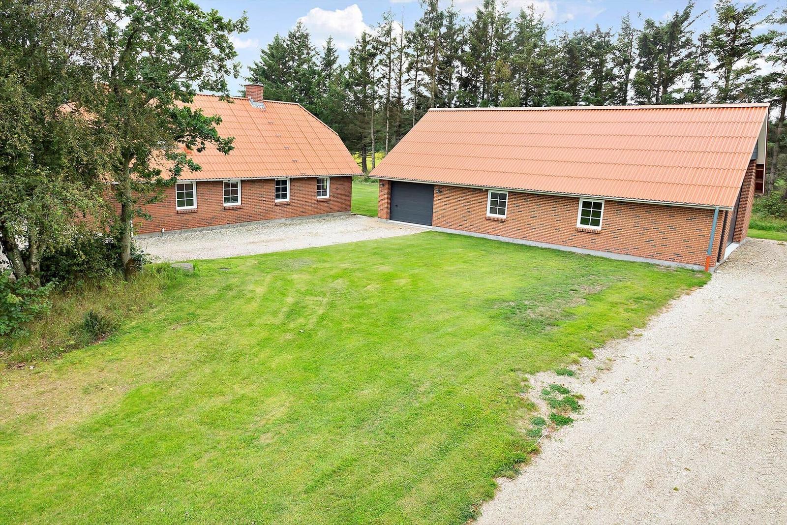 Zwei Backsteinhäuser mit rotem Dach, grüner Wiese und Wald im Hintergrund.