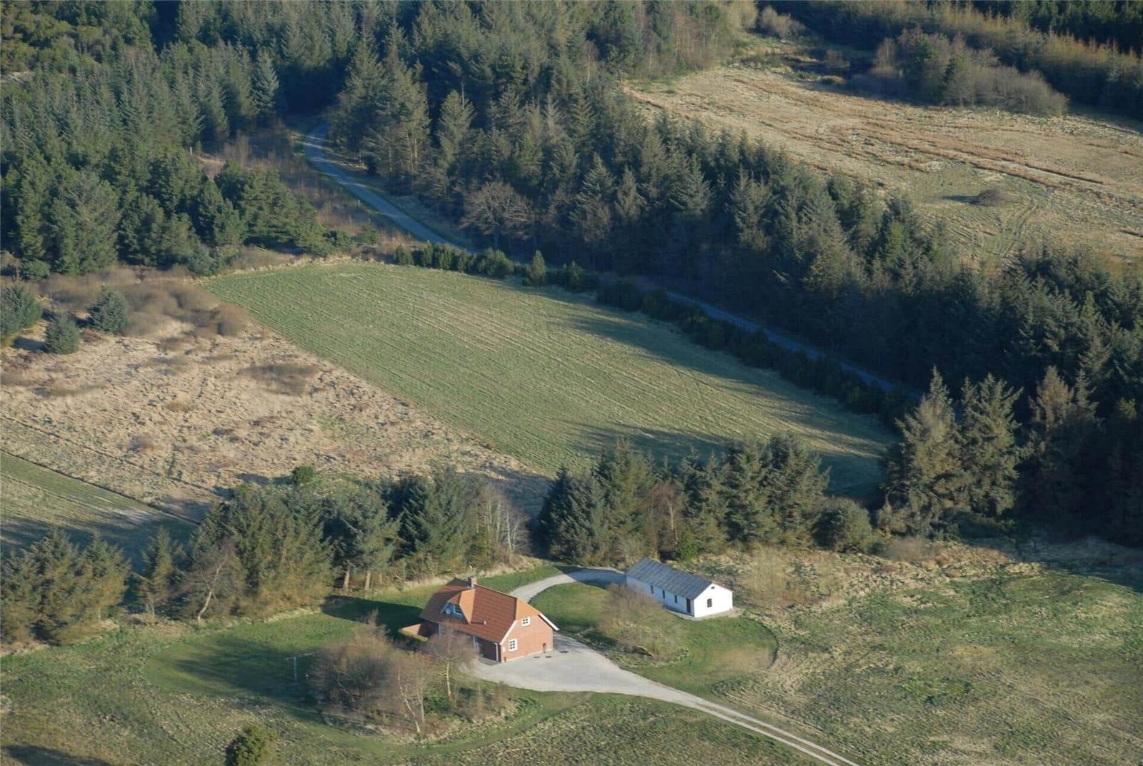 Haus mit rotem Dach und weißem Nebengebäude in ländlicher Umgebung mit Wiesen und Wald.