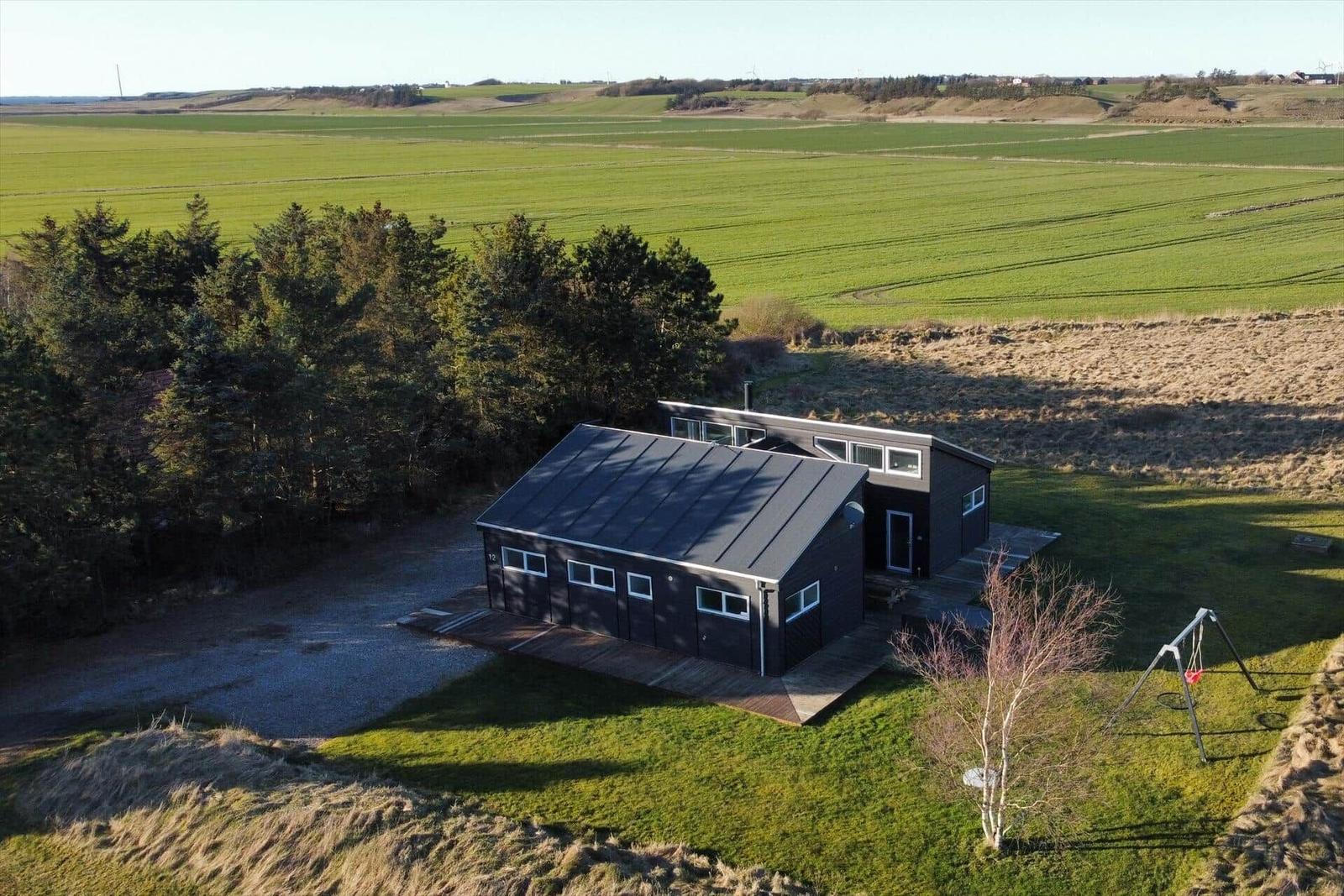 Black holiday home with wooden terrace and garden. Satellite dish on the wall.