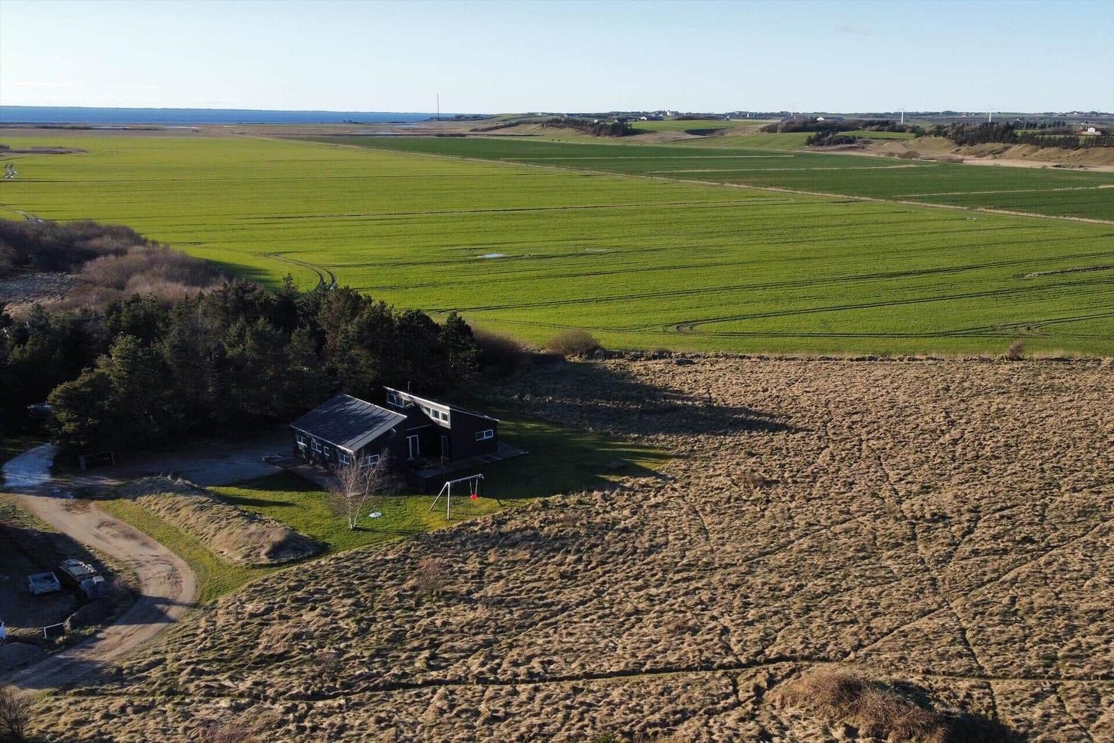 Three houses with wooden cladding and roof on green property with forest and sea view.