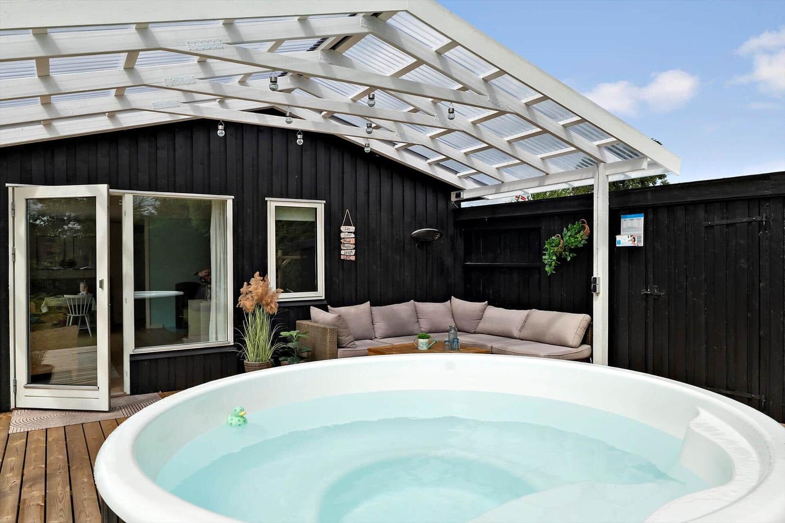 Black wooden house with terrace, hot tub, and seating area in the garden.