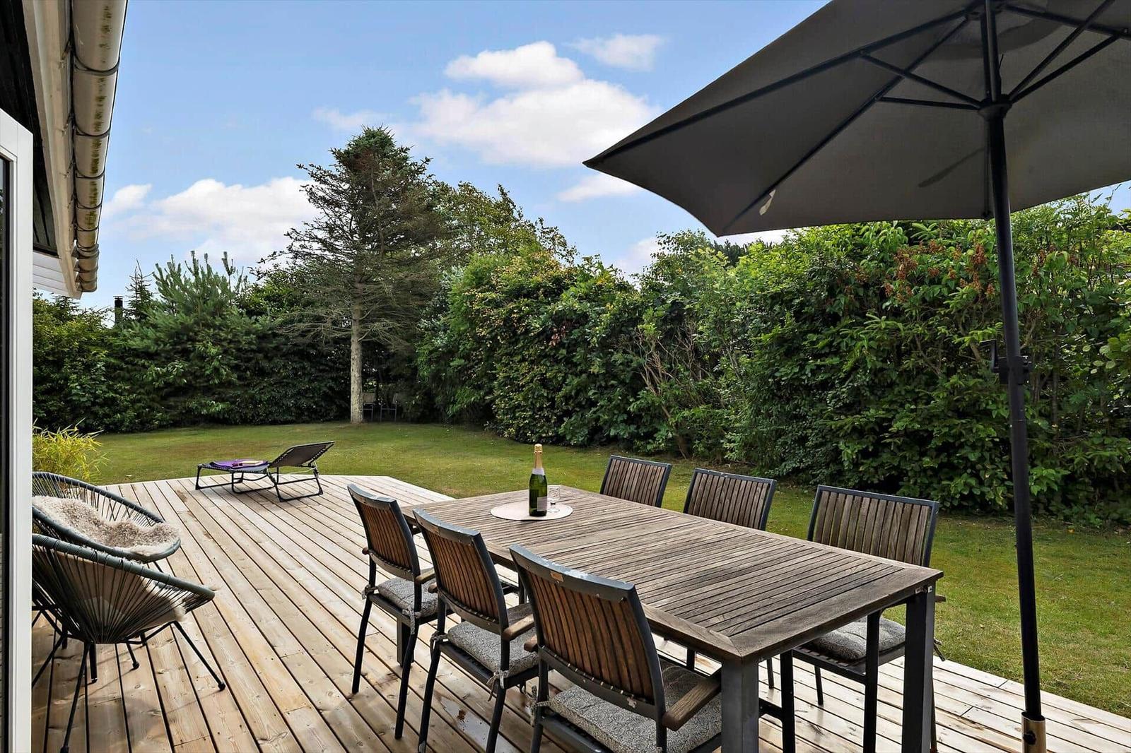 Black house with terrace, lounge chair, hot tub, and garden.