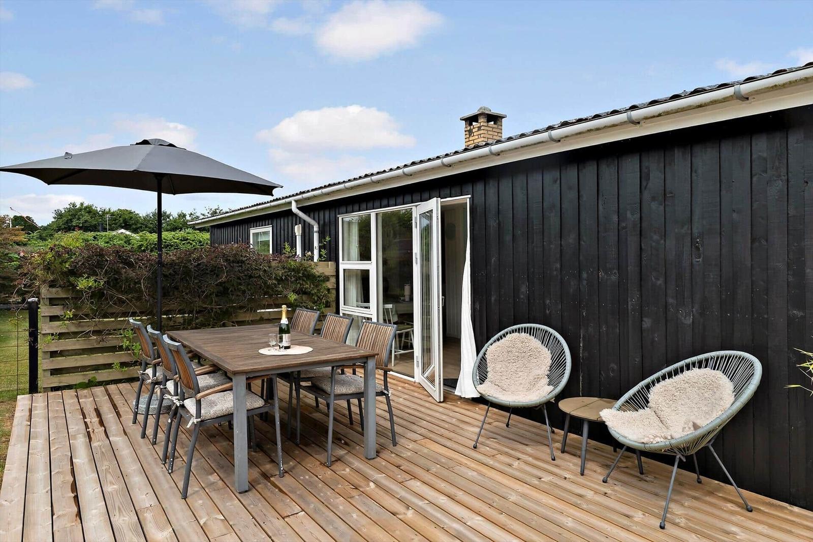 Terrace with seating group, wooden table, and plants in front of black wooden house