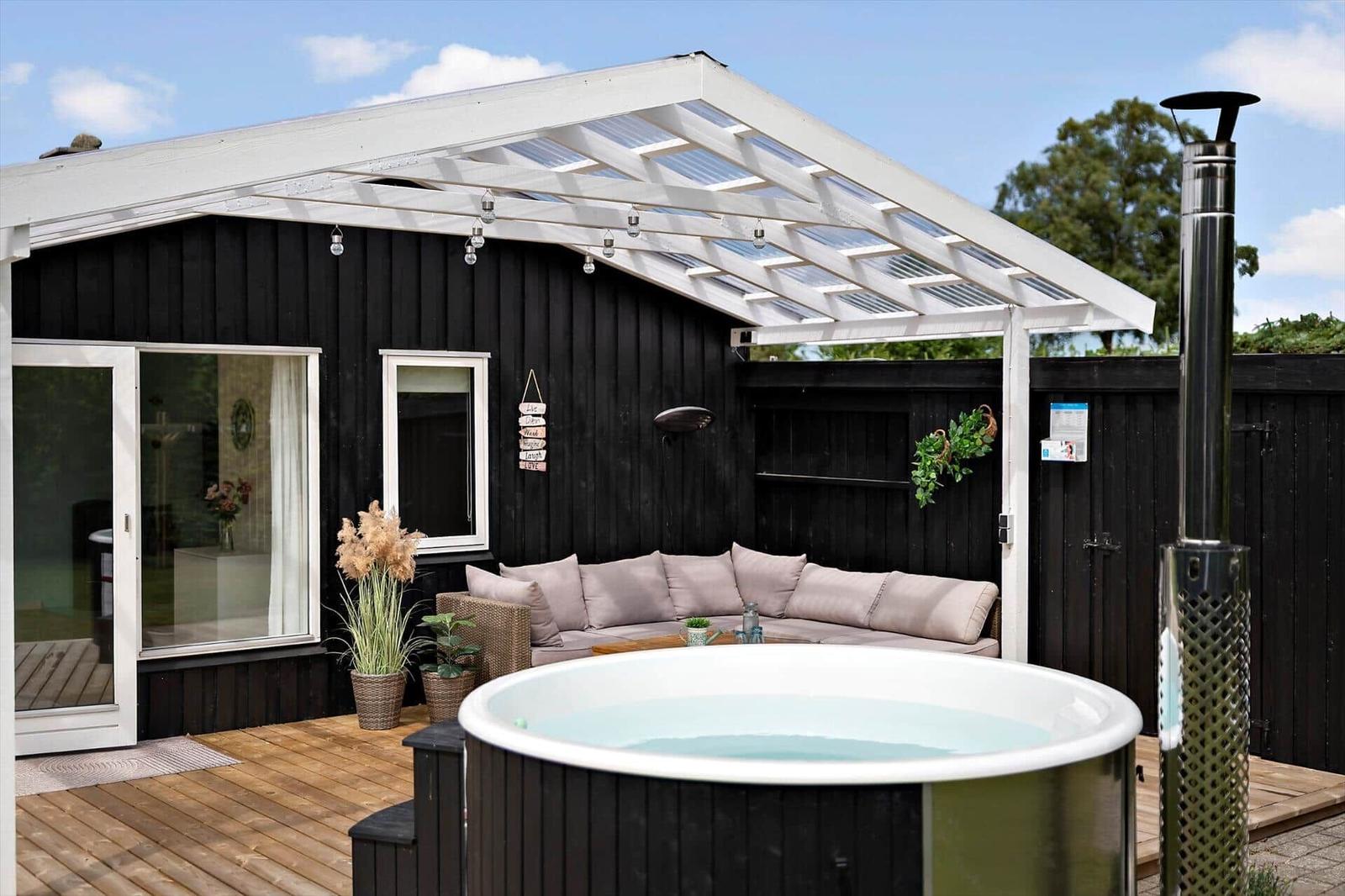 Deck with lounge chair, seating area, and dining table. Black house with white windows.