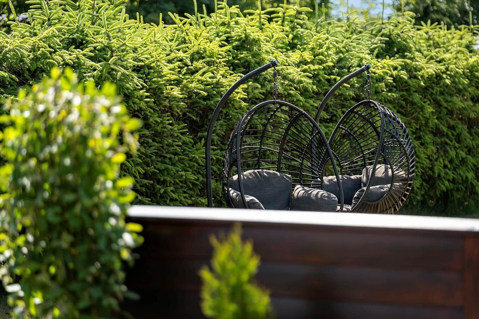 Terrasse mit Sitzgruppe, Tisch und Stühlen. Hintergrund: Holzwand und grüne Hecke.