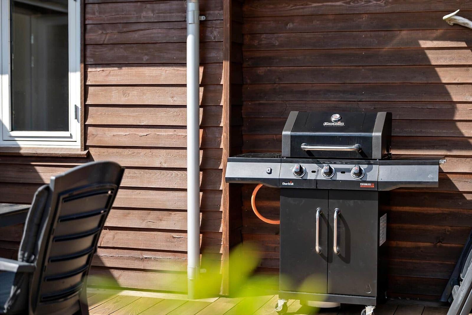 Terrasse mit Tisch, Stühlen und Pflanze. Holzgeländer und grüne Bäume im Hintergrund.