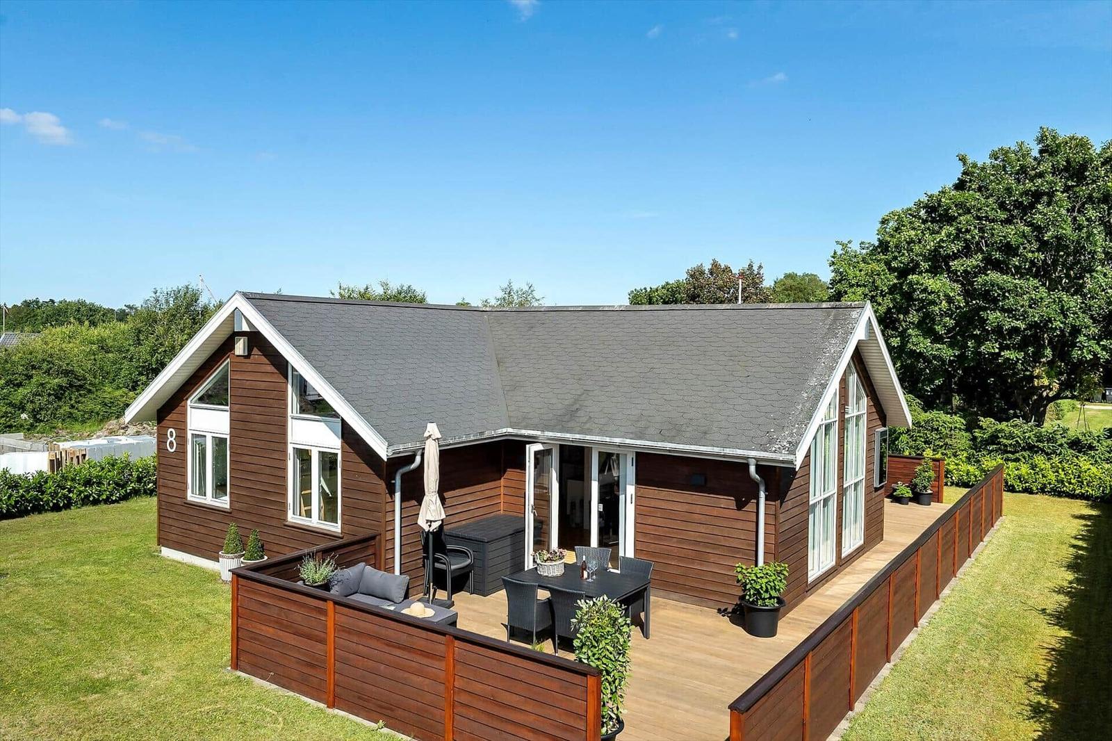 Holzhaus mit Terrasse und großem Garten. Hinterhof mit Hecke und weiteren Häusern.