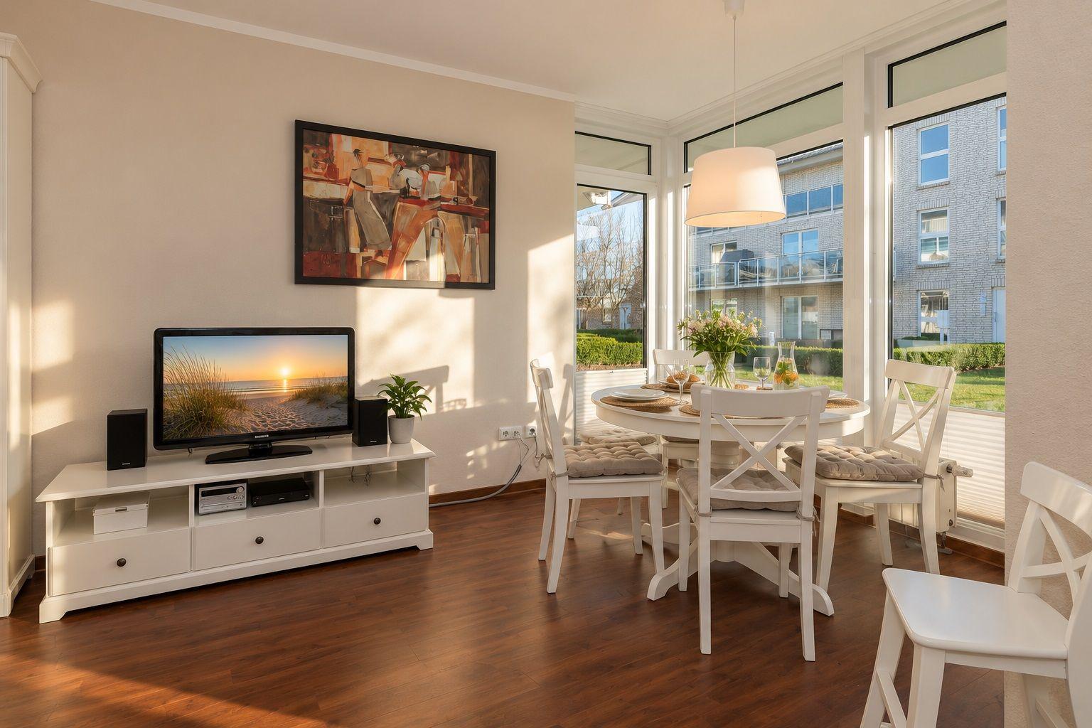 Wohnzimmer mit Sofa, Fernseher und Essbereich. Durchgang zum Balkon mit Gartenansicht.
