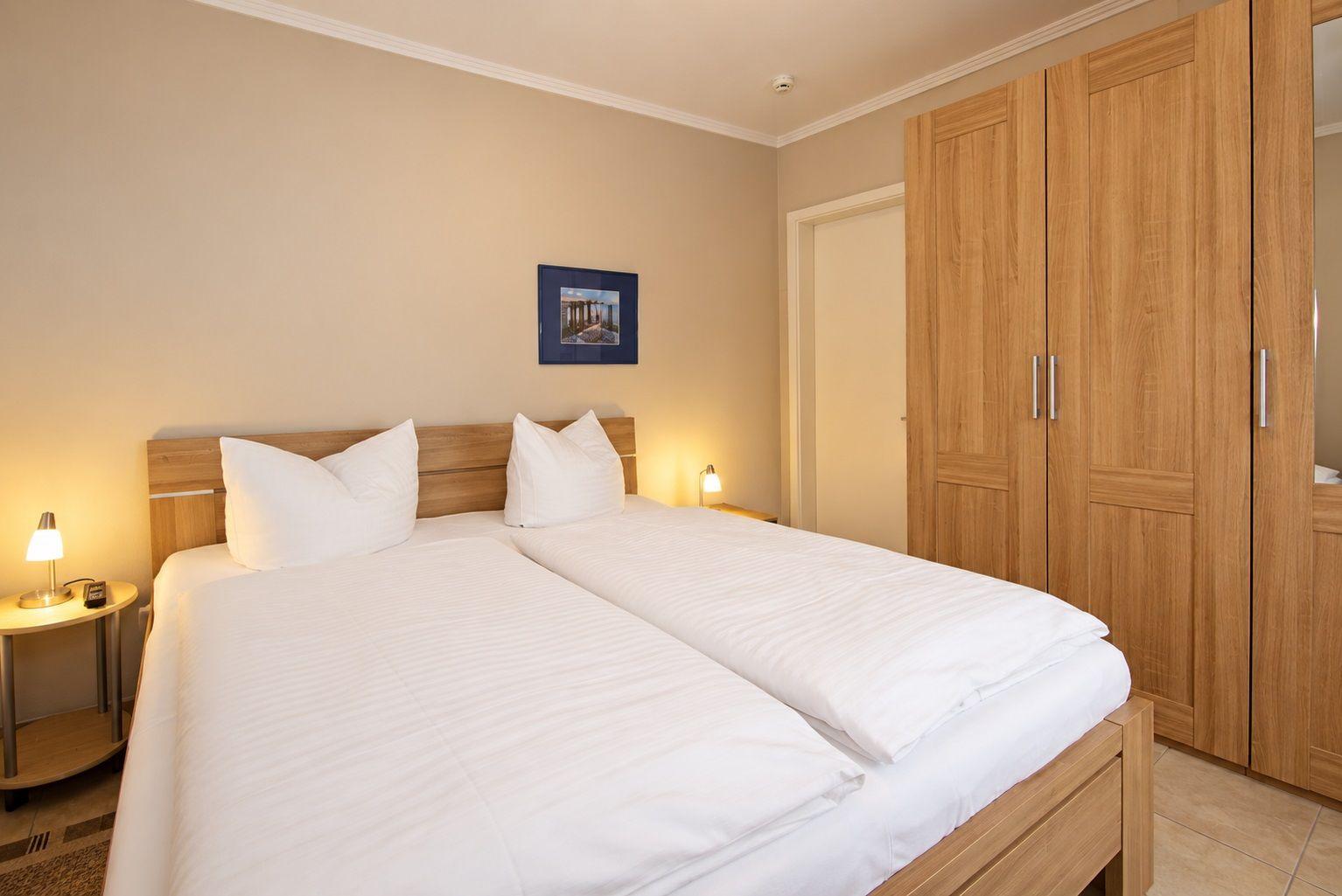 Schlafzimmer mit Doppelbett, Holzschrank und Nachttisch mit Lampe.