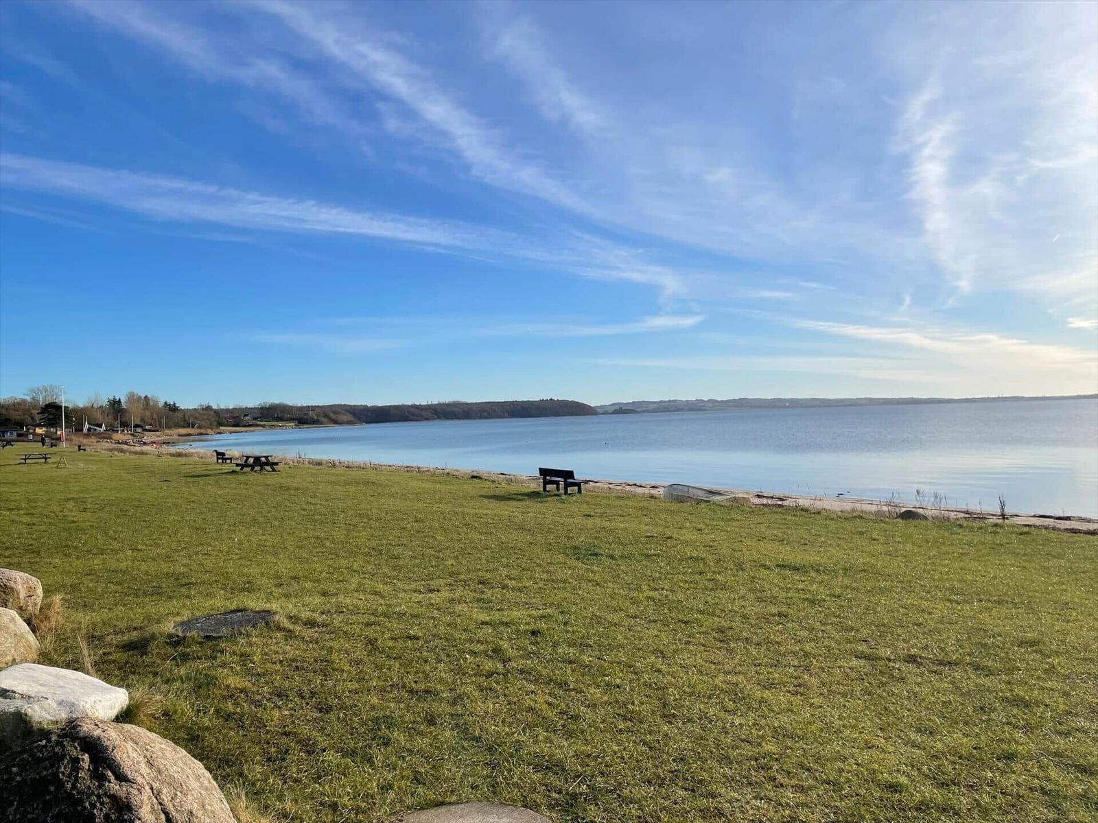 Grüner Rasenbereich am Wasser mit Bank und Picknicktisch unter blauem Himmel.