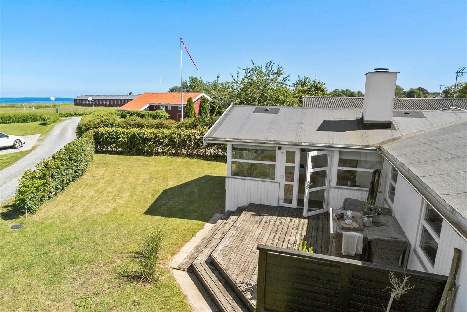 Haus mit Terrasse, Garten und Blick auf grüne Bäume unter blauem Himmel.