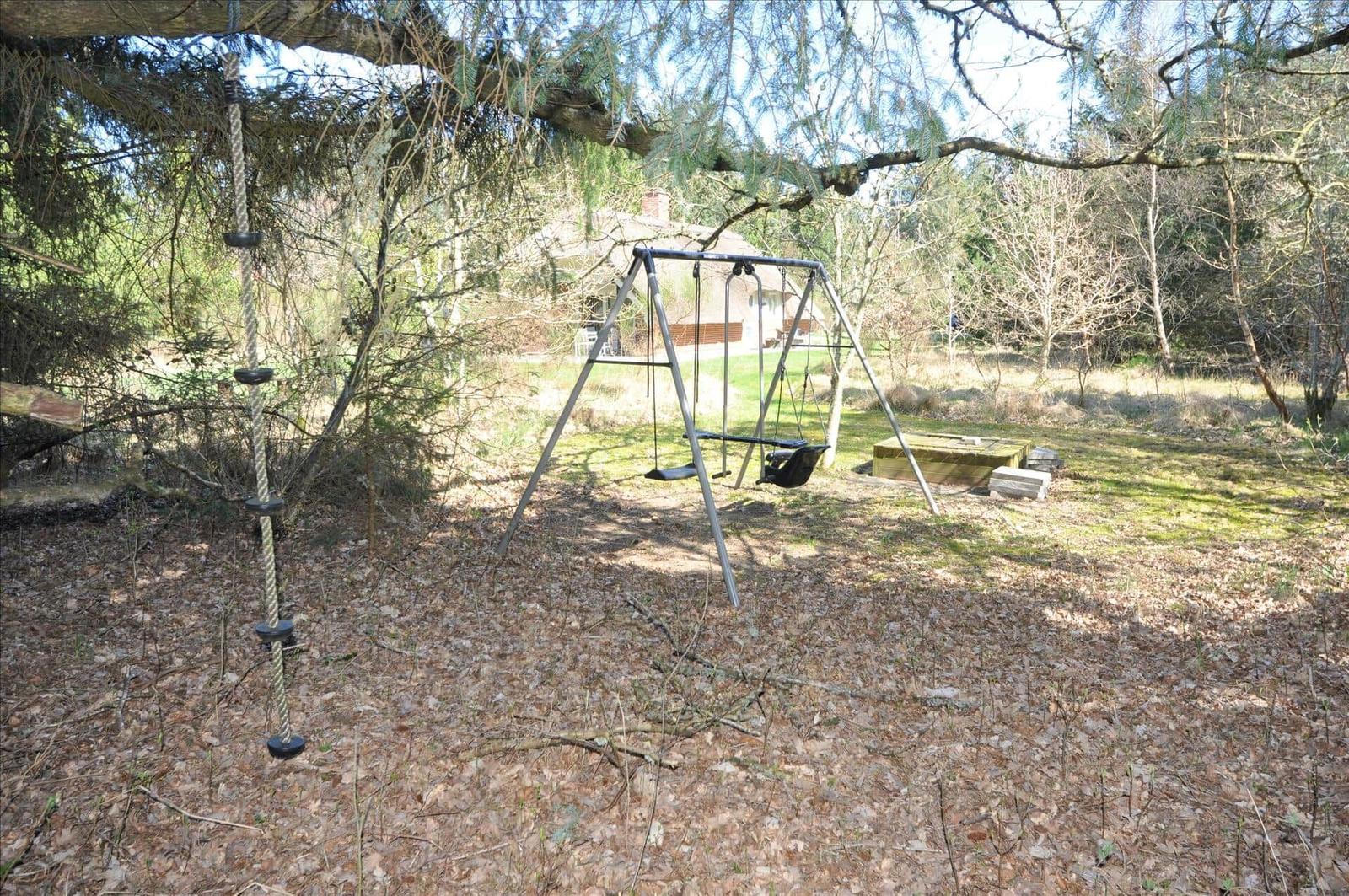 Haus mit Strohdach, Gartenbereich mit Liegestühlen und Grill, umgeben von Bäumen.