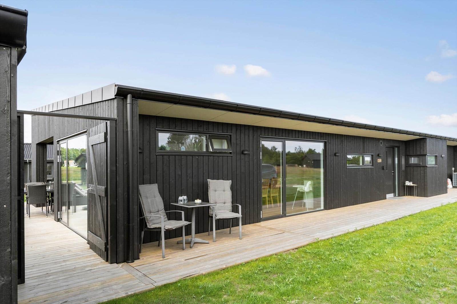 Moderne schwarze Villa mit Spielplatz und grünem Rasen unter blauem Himmel.