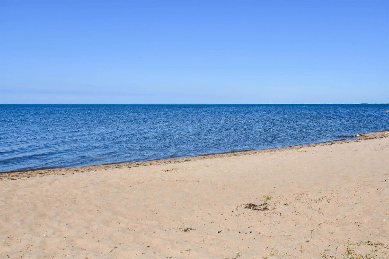 Beach with dunes, green areas, and houses under blue sky.