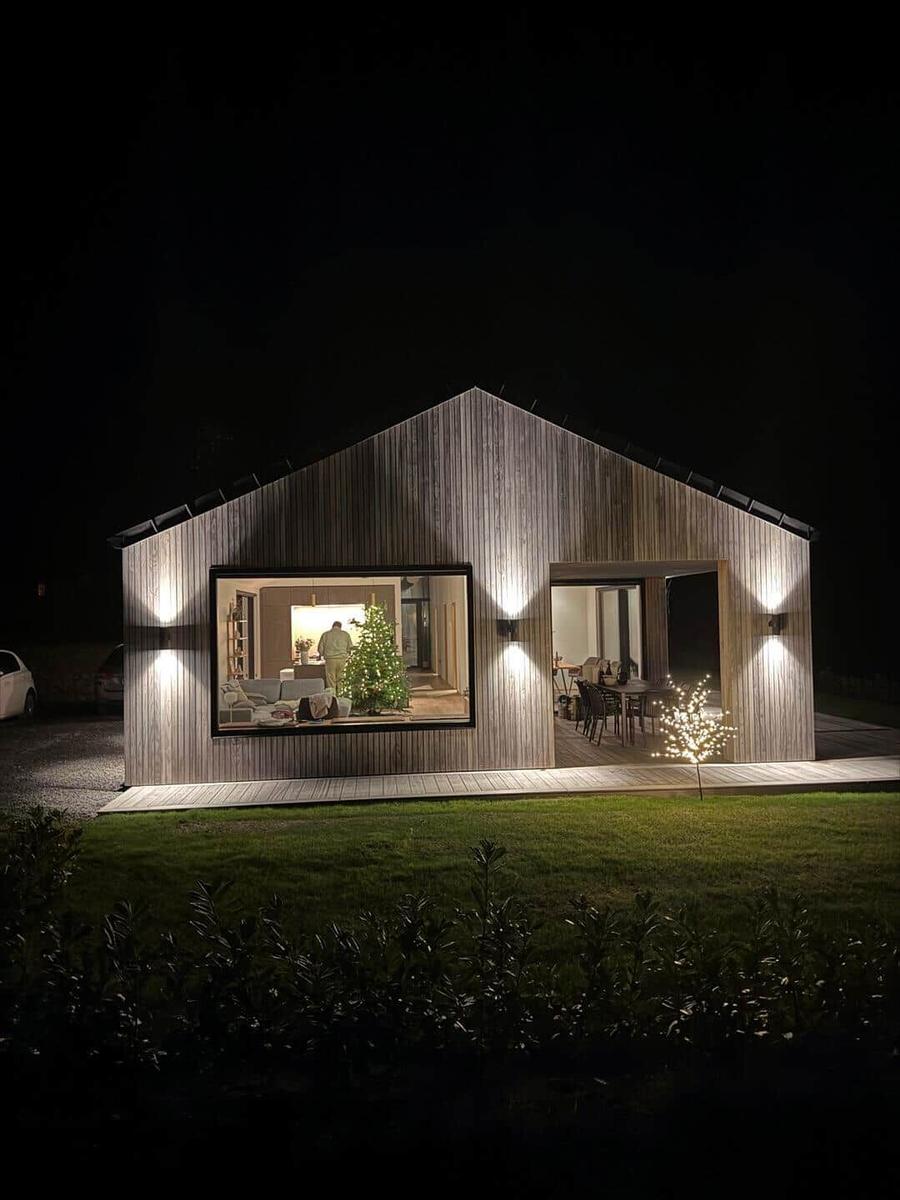 Moderne Holzhütte mit beleuchtetem Innenraum und Weihnachtsbaum. Außenbereich mit Tisch und Stühlen.