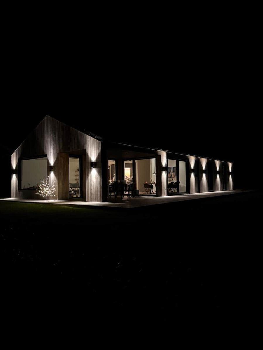 Moderne Villa mit Holzfassade und beleuchteten Fenstern bei Nacht.