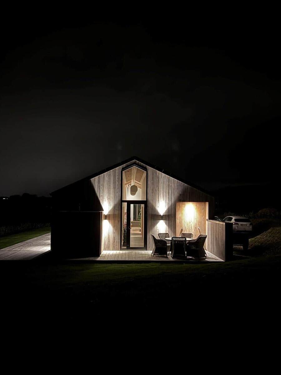 Moderne Holzhütte mit beleuchtetem Eingang und Außentisch im Dunkeln.