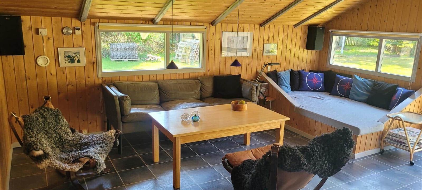 Living room with wood walls, sofa, windows, and glass door to the garden.