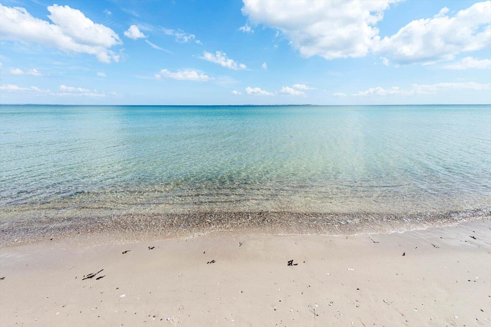 Strand mit weißen Sand, Ferienhäuser und Campingplatz in grüner Landschaft.