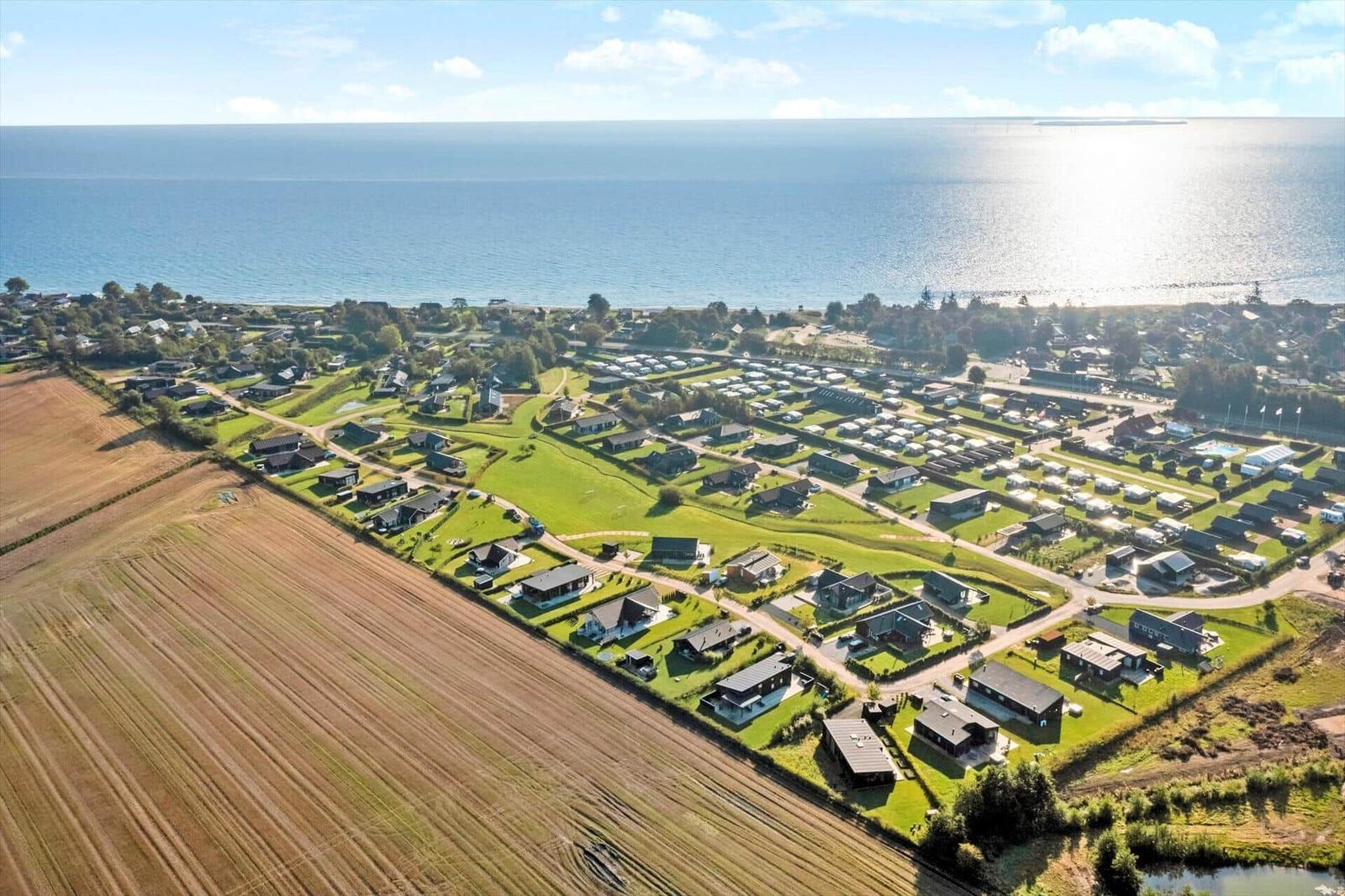 Strand mit weißem Sand, rotem und weißem Leuchtturm, gelbem Pickup und Ferienhaus im Hintergrund.