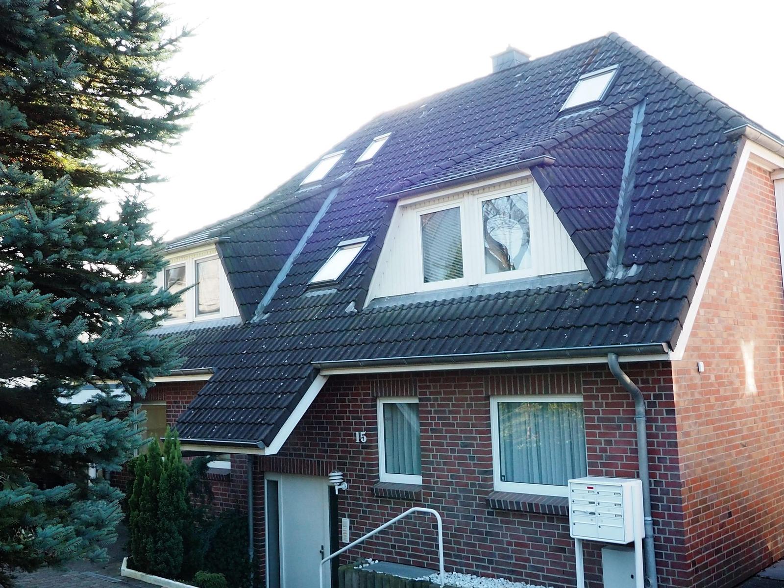 Zweistöckiges Haus mit Balkonen und Garten. Roter Ziegelbau unter blauem Himmel.