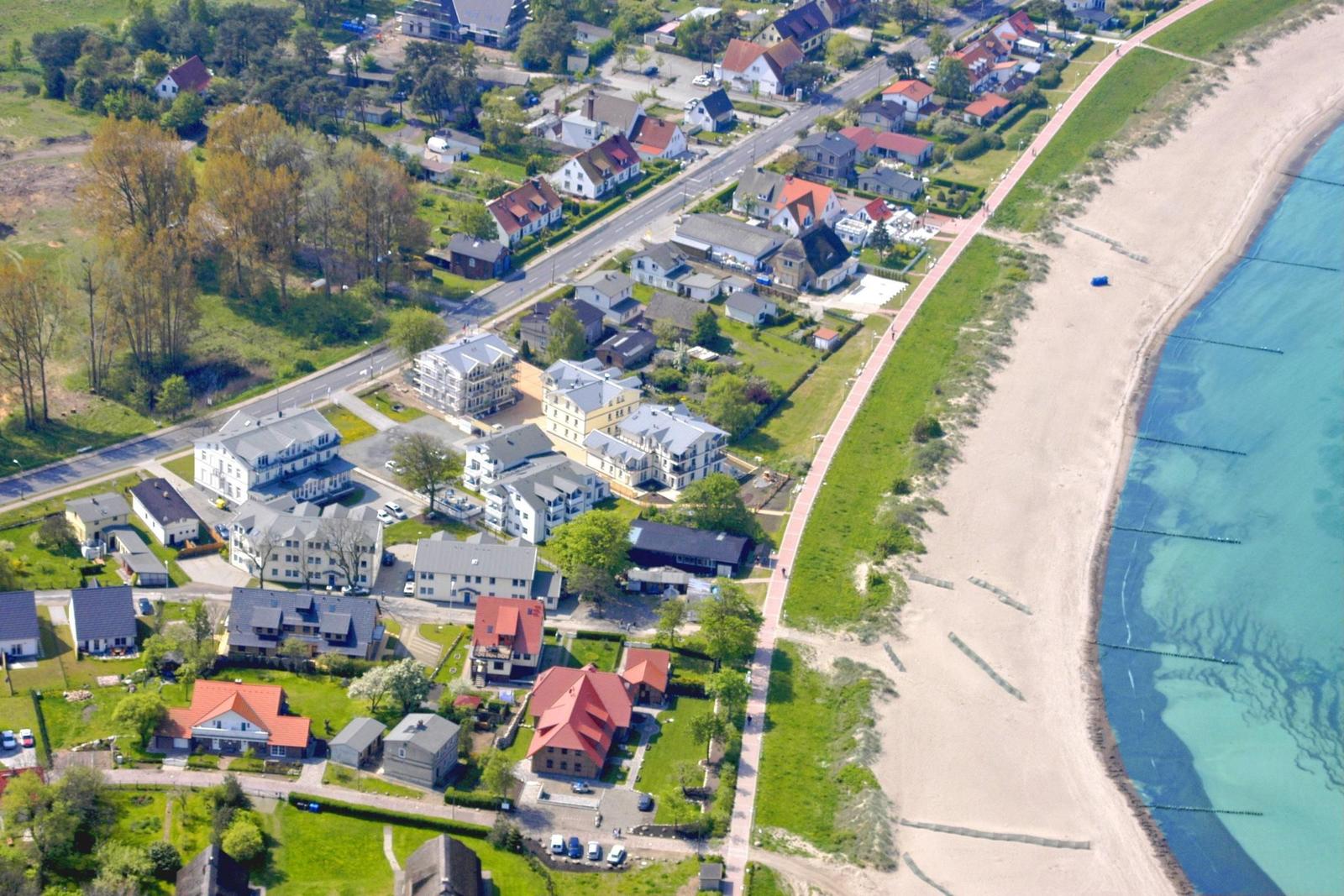 Strand mit Badegästen, grüne Vegetation und kleines Haus im Vordergrund.