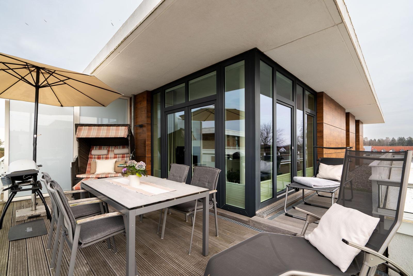 Terrace with table, chairs, and umbrella. View of the sea and modern buildings.