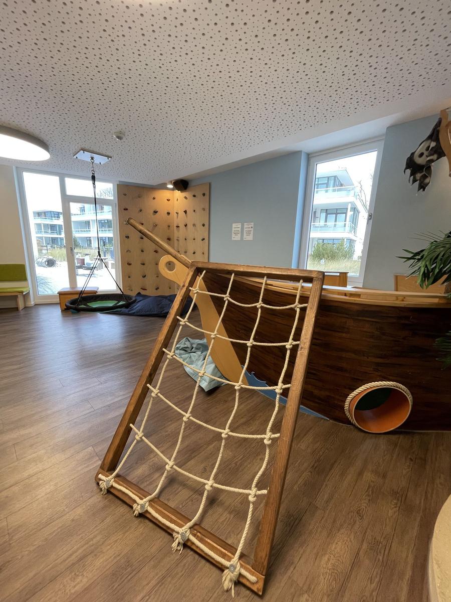 Ein großer Schaukelhängematten mit grünem Innenfutter hängt in einem Raum mit Holzboden und Kinderspielplatz.