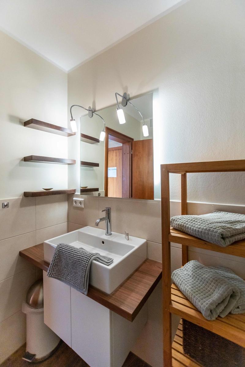 Balkon mit weißen Stühlen und Blick in das Schlafzimmer mit Bett und Fenster.