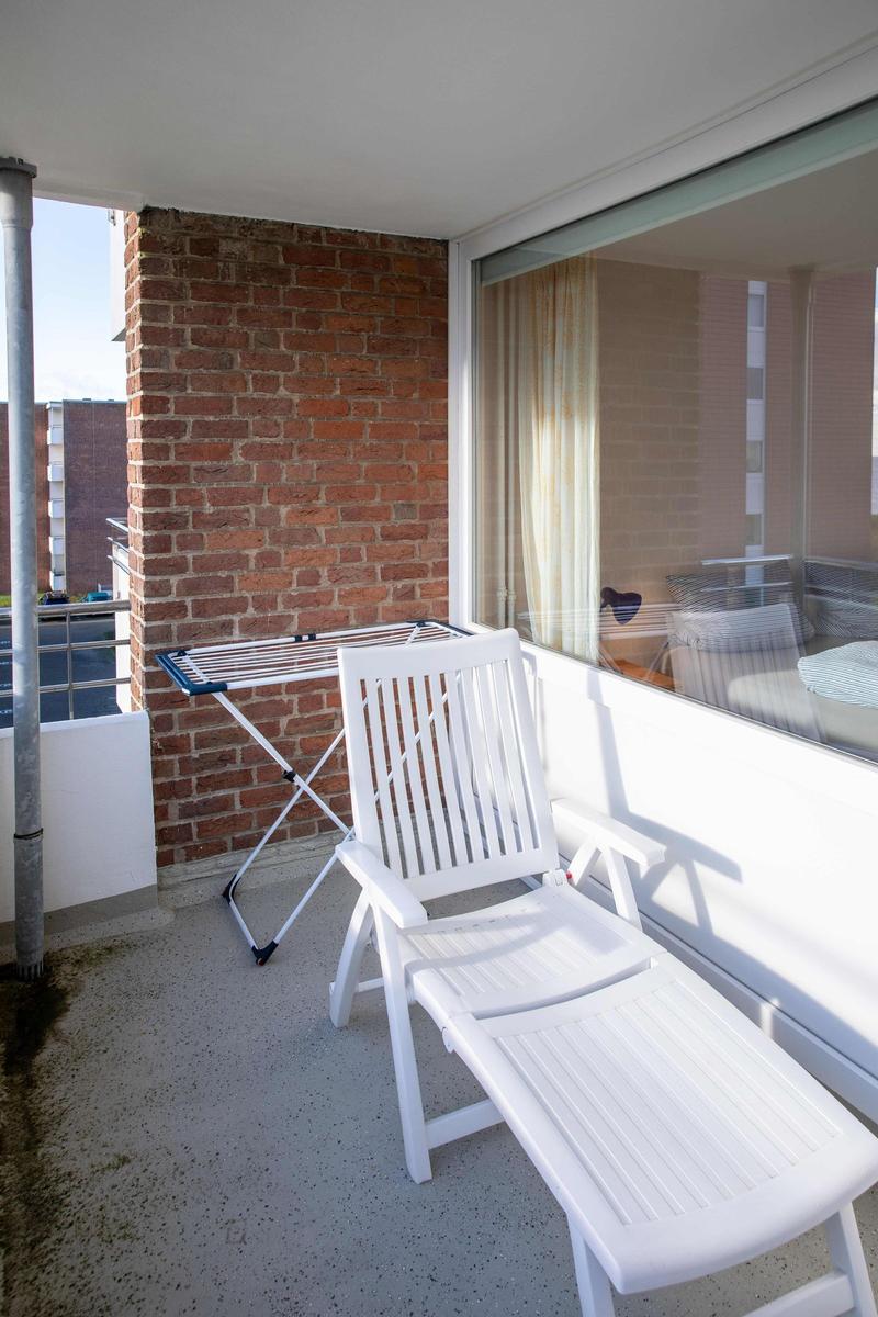 Terrasse mit grünen Stühlen und Tisch, Blick auf Gebäude und Bäume.