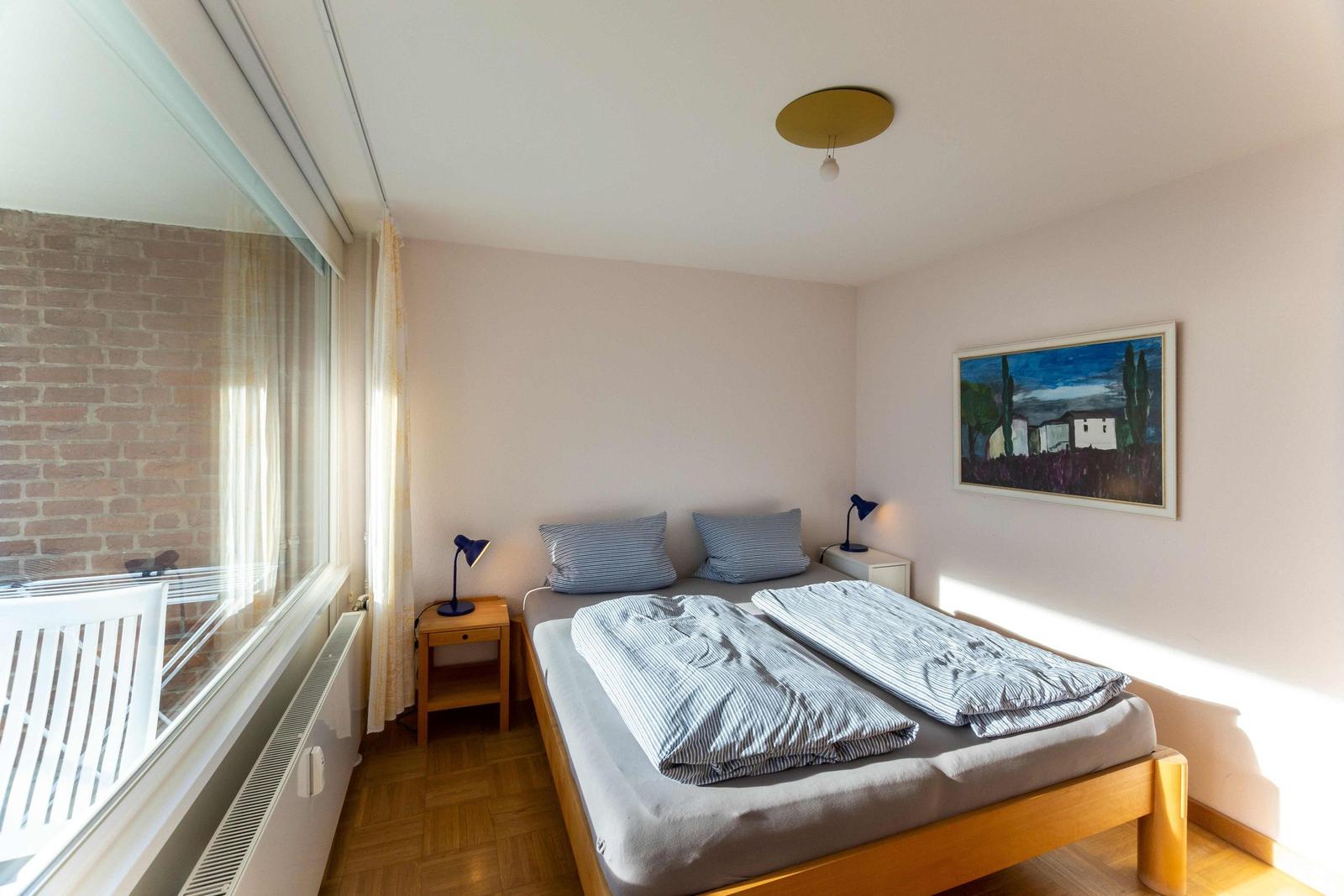 Schlafzimmer mit Blick aufs Meer und Balkon. Bett, Nachttisch und Lampe sind sichtbar.