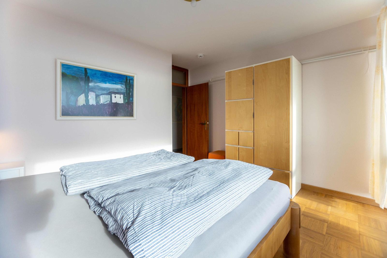 Schlafzimmer mit Balkonblick aufs Meer. Bett mit Streifenbezug und zwei Nachttische.