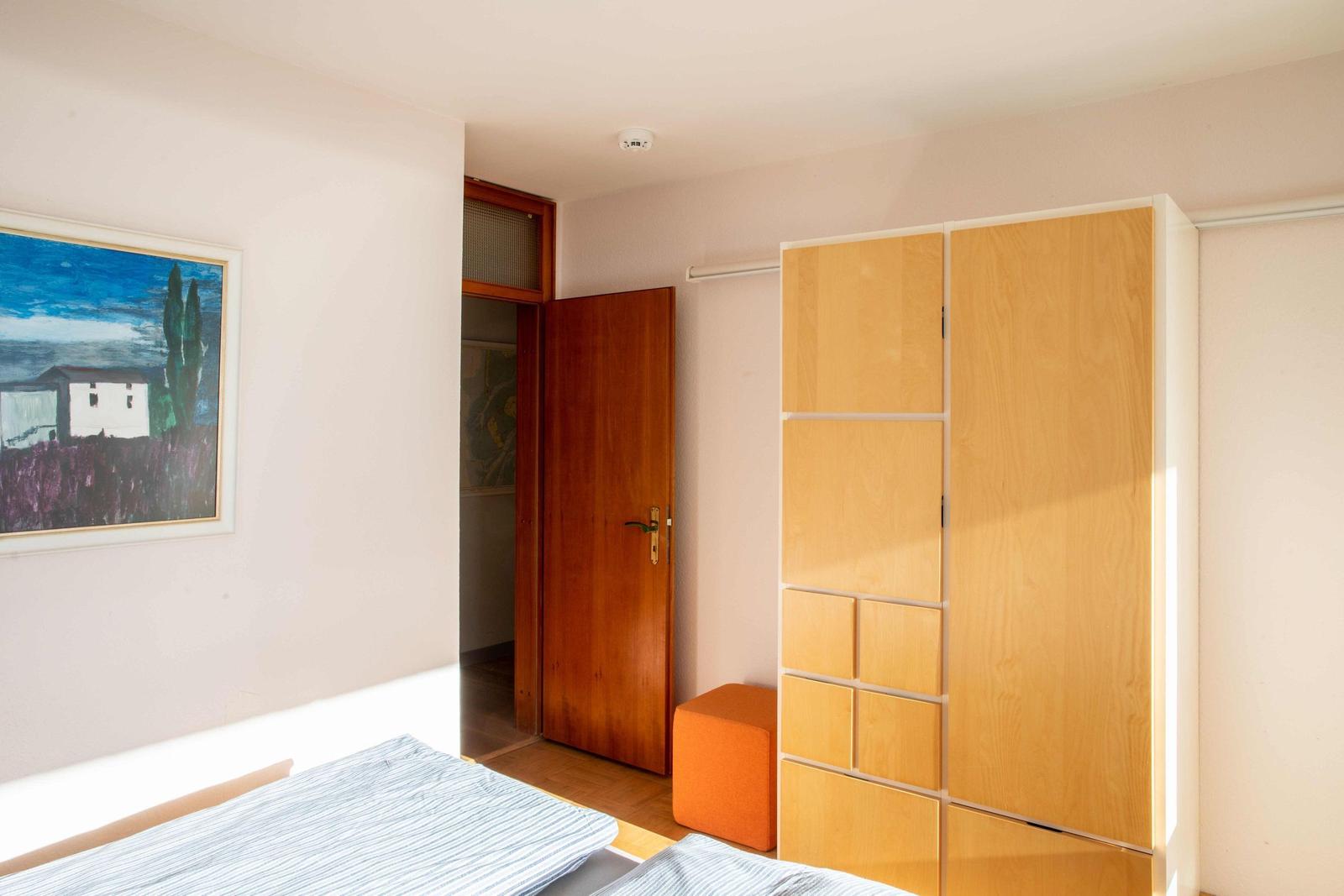 Schlafzimmer mit Holzbett, zwei Bildern und Fenster mit Vorhang.