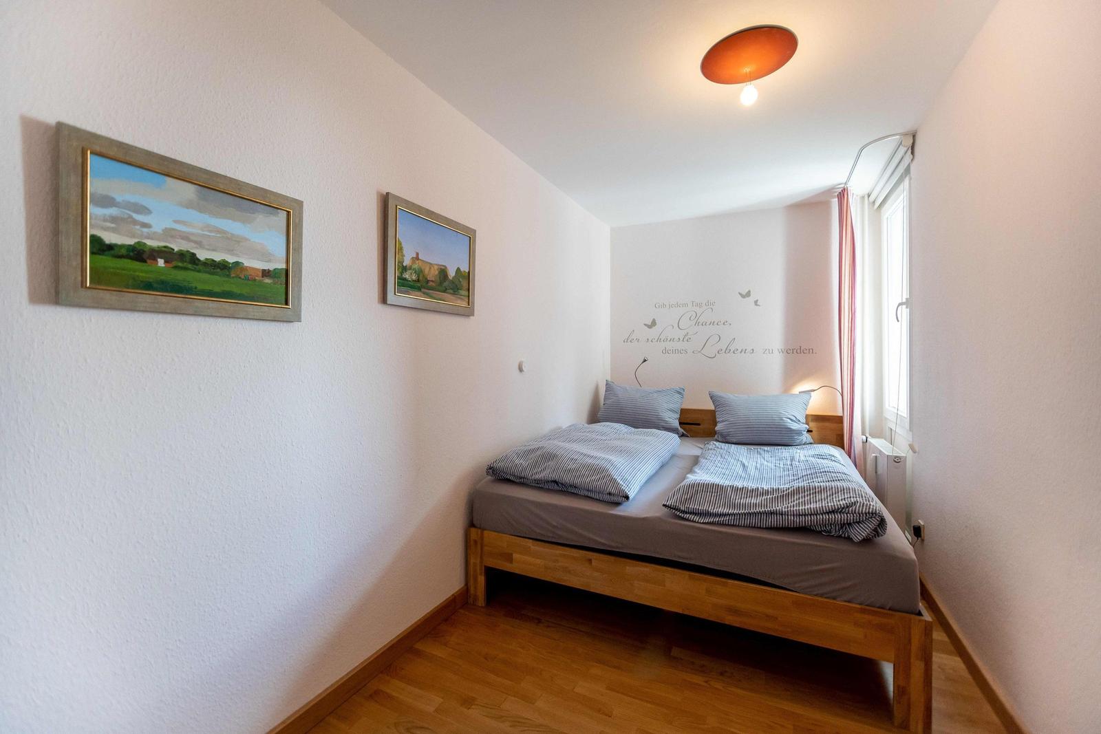 Schlafzimmer mit Doppelbett, Wandbild und Fenster mit Vorhängen.