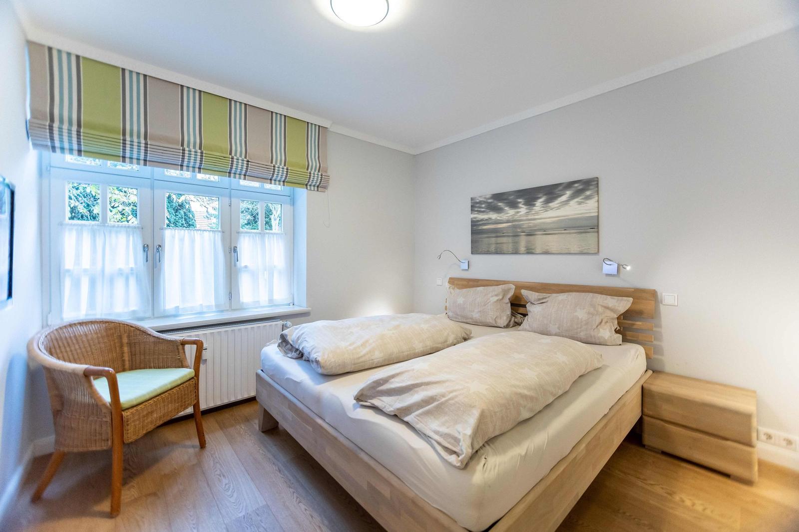 Schlafzimmer mit Doppelbett, Holzkopfteil und Wandbild. Weiße Schränke an der Wand.