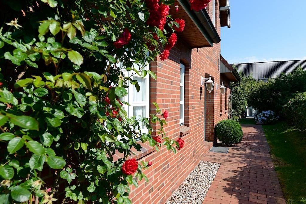 Rotes Backsteingebäude mit weißer Tür und Fenstern. Vorgarten mit Rasen, Bäumen und einer weißen Bank.