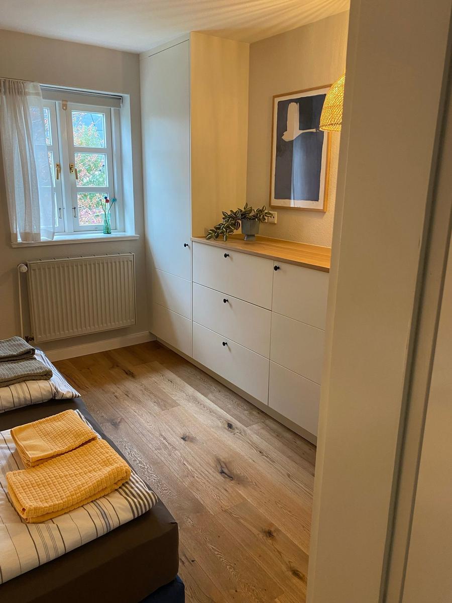 Essbereich mit runden Tisch, grünen Stühlen und Küchenbereich mit weißen Schränken.