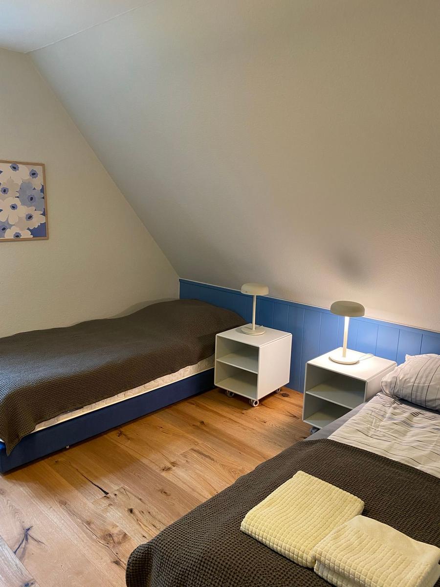 Zimmer mit Doppelbett, Holzboden und Fenster mit Blick auf Bäume.