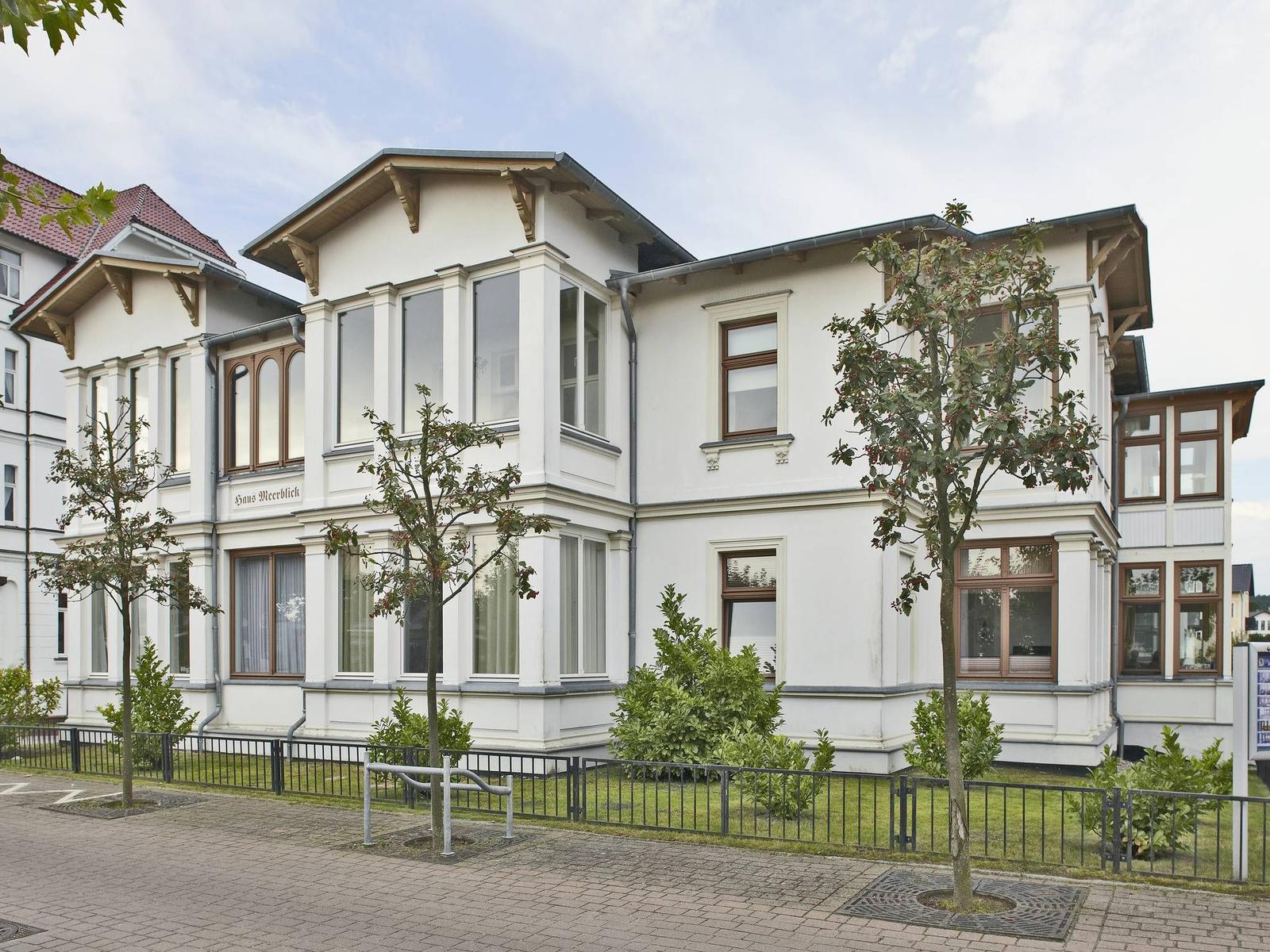 Haus Meerblick mit weißen Wänden, braunen Fensterrahmen und kleinem Garten.
