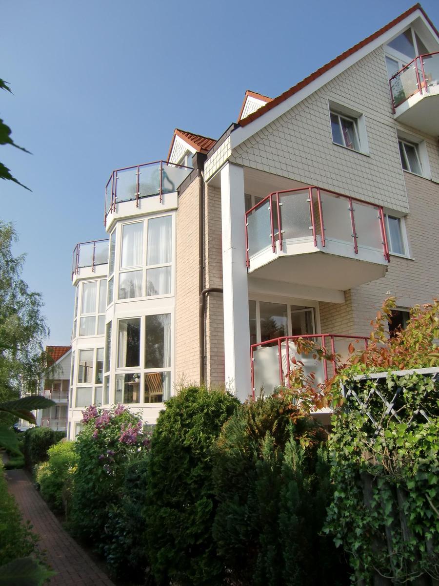 Modernes Mehrfamilienhaus mit Balkonen und rotem Dach unter blauem Himmel.