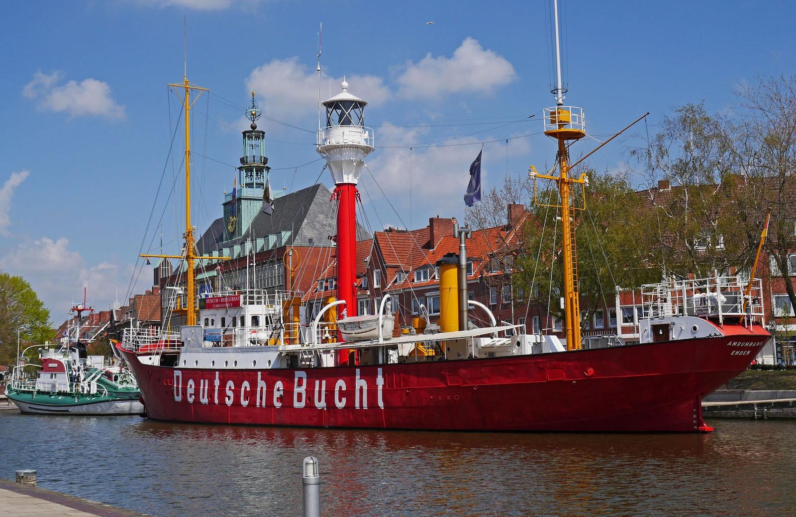 Zwei Windmühlen stehen am Ufer eines Flusses, umgeben von Bäumen und Gras.