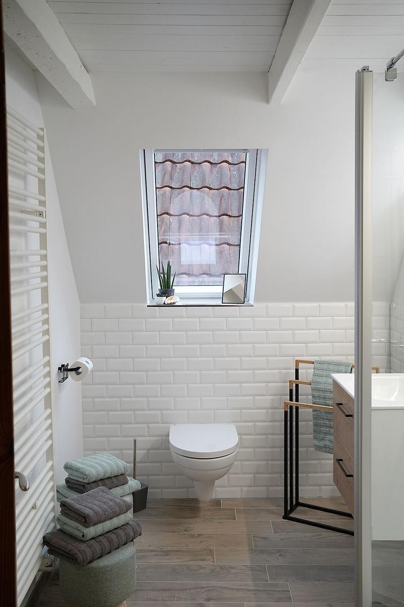 Badezimmer mit Toilette, Handtuchständer und gefalteten Handtüchern auf Stühlen.
