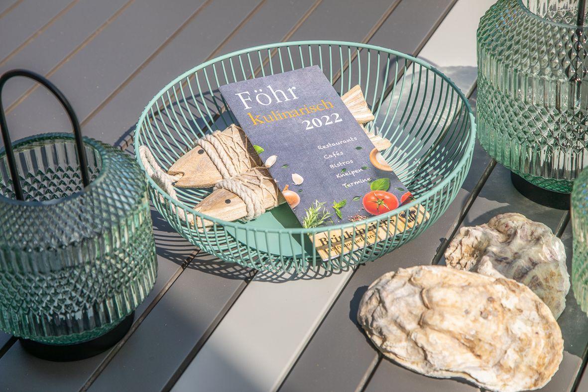 Terrasse mit Tisch und Stühlen neben Backsteinhaus mit Pflanzen im Vordergrund.
