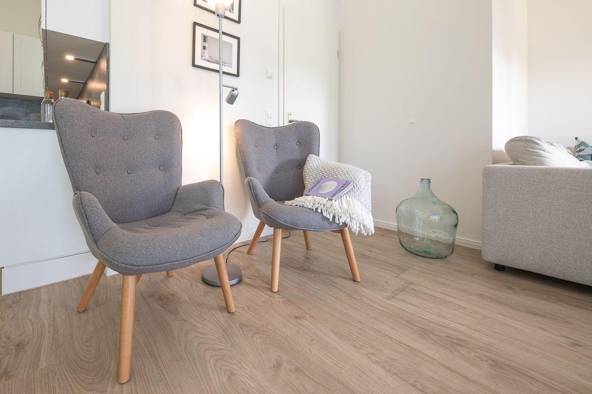 Ein grauer Sessel mit Kissen und Decke steht in einem Raum mit weißen Wänden und einem weißen Regal.