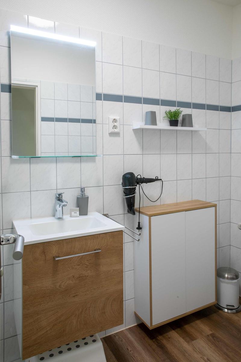 Badezimmer mit Dusche, Waschbecken und Spiegelschrank. Fenster mit Vorhang.