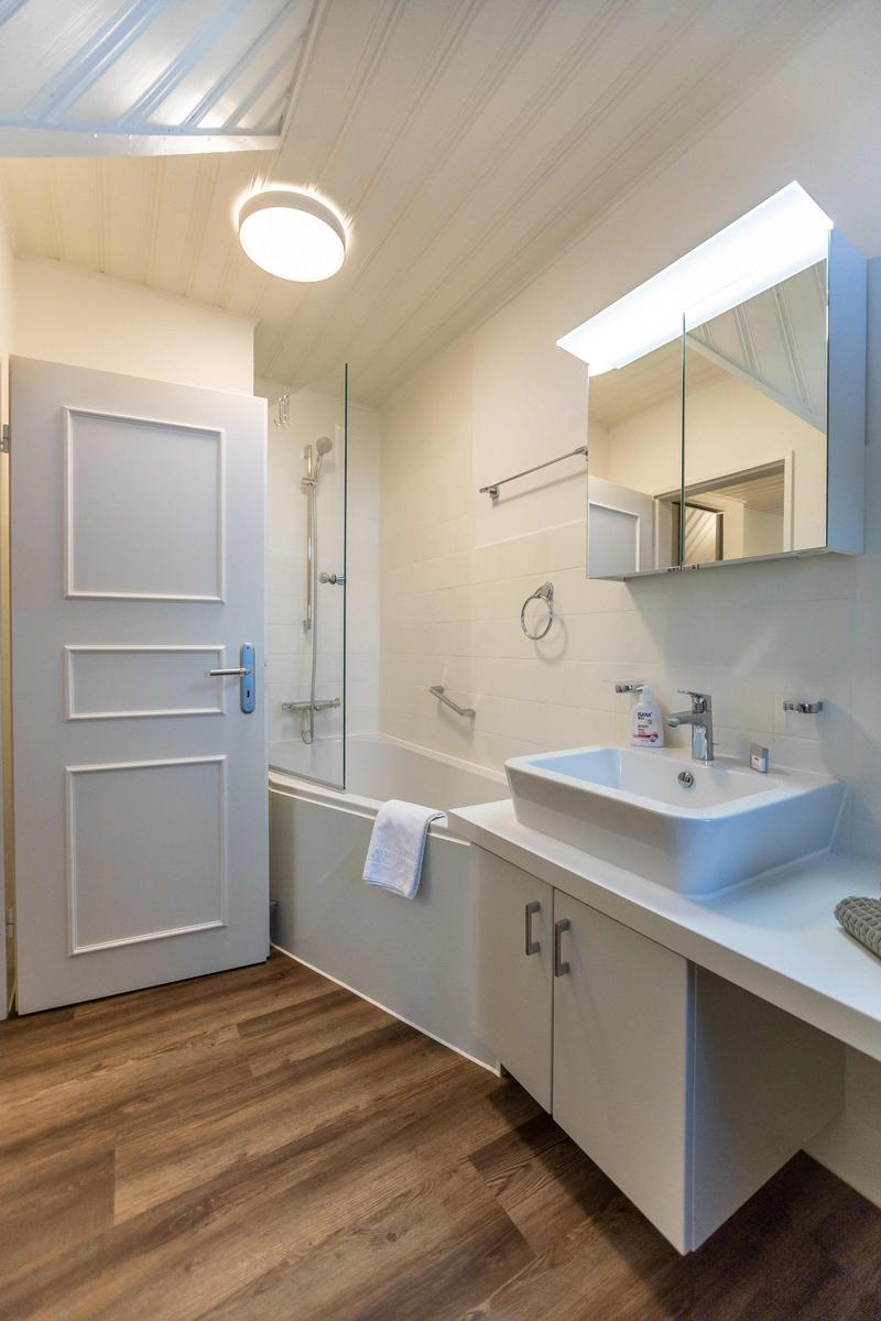 Badezimmer mit Waschbecken, Spiegelschrank und Dusche. Fenster mit Vorhang und Pflanze.