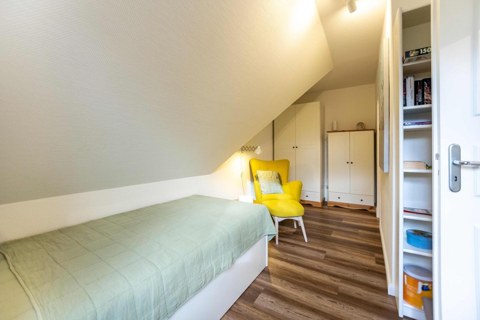 Schlafzimmer mit Dachschrägen, Bett, Fenster, Stuhl und Schrank.